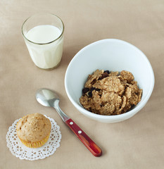 bowl of cornflakes, muffin and glass of milk on beige tablecloth