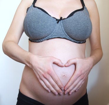 Pregnant woman with hands on her belly forming a heart