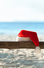 Red Santa's hat on wooden bench at the tropical beach