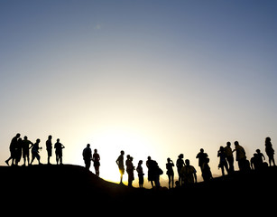Naklejka na ściany i meble Group of people silhouetted against the sun on top of a mountain