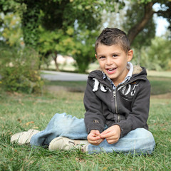 Jeune garçon assis dans l'herbe, heureux et souriant