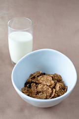 bowl of cornflakes and glass of milk on beige tablecloth
