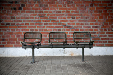bench with three seats in front of a brick wall