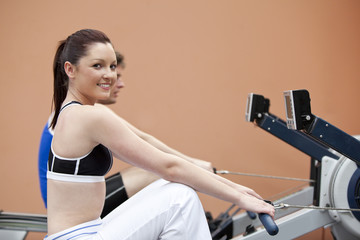 Happy woman with her boyfriend using a rower in a fitness centre