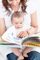 Happy mother showing a book to her baby sitting in the sofa