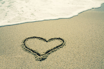 handwritten heart on sand with wave approaching