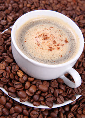 Cup of coffee sprinkled with cinnamon with coffee beans around
