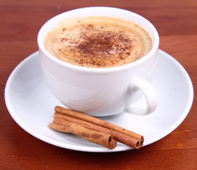 Cup of coffee sprinkled with cinnamon and with cinnamon sticks