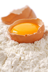 Broken egg with shells on flour, white backdrop