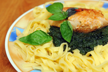 Fried chicken breast with spinach and pasta and a leaf of basil