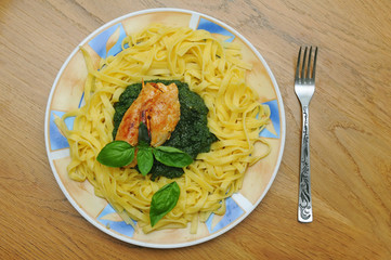 Fried chicken breast with spinach and pasta and a leaf of basil