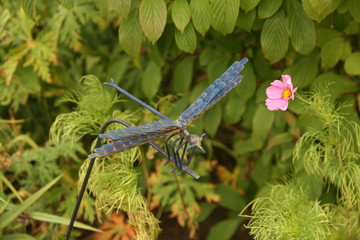 Dragonfly garden ornament and pink flower against bushes