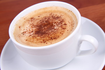 Cup of coffee sprinkled with cinnamon on wooden table