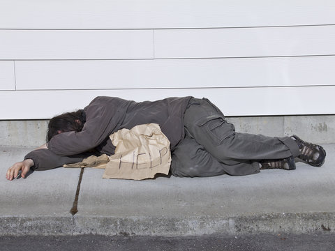 Poor man lying on sidewalk with help sign