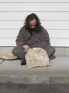 Poor man sitting on sidewalk with help sign
