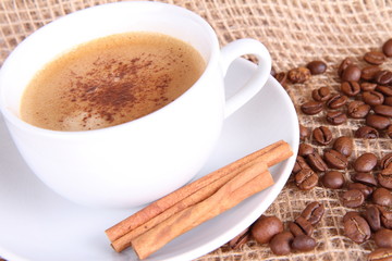 Cup of coffee with cinnamon sticks, coffee beans and burlap
