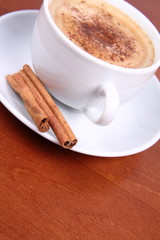 Cup of coffee sprinkled with cinnamon and with cinnamon sticks