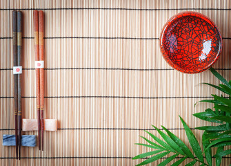 Chopsticks, spoon and red bowl on bamboo background