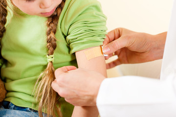 Kinderarzt klebt Kind ein Pflaster auf