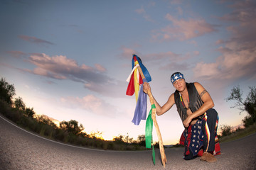 Indigenous man in the middle of a road with ceremonial pole and