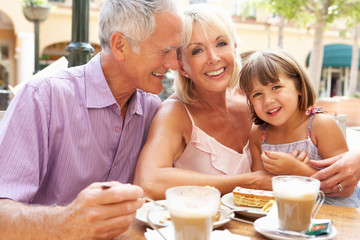 Grandparents With Granddaughter Enjoying Coffee And Cake In Cafe
