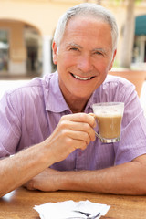 Fototapeta na wymiar Senior Man Enjoying Coffee And Cake In Cafe