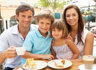 Young Family Enjoying Cup Of Coffee And Cake In Cafe Together