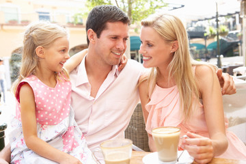 Young Family Enjoying Cup Of Coffee In Cafe Together