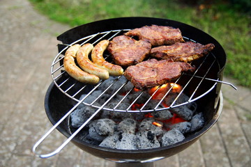 Grill mit Grillfleisch und Bratwurst im Garten