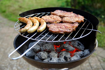 Grill mit Grillfleisch und Bratwurst im Garten
