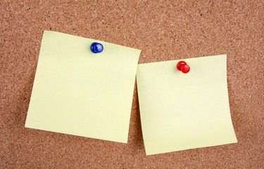 two yellow memo sticks with pins on cork board