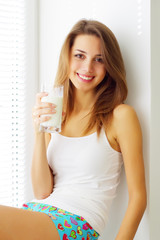 Smiling girl sitting by the window and drink milk