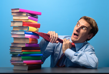man at the table looking with fear at a stack of colored books