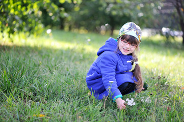 Nice little girl in blue coat pick up flowers in autumn park