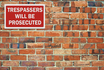 'Trespassers' will be prosecuted' sign, against brick wall. Spac