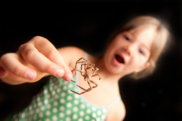 young girl holding a brown spider by leg and surprised