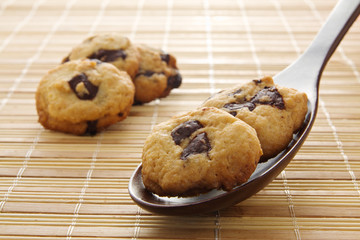 Several chocolate chip cookie, two on a wooden spoon