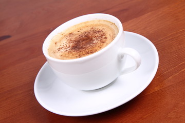 Cup of coffee sprinkled with cinnamon on wooden table