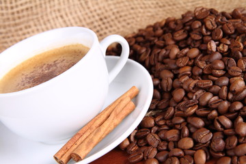 Cup of coffee with cinnamon sticks, coffee beans and burlap