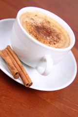 Cup of coffee sprinkled with cinnamon and with cinnamon sticks