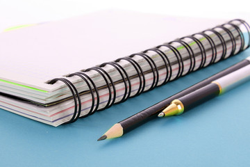 Notepad, pencil and pen on blue background