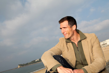 Smiling man sitting by the beach in autumn