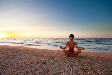 Fototapeta na wymiar Teen boy at the beach meditating on sunset
