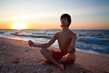 Teen boy at the beach meditating on sunset
