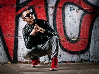 Young man sits against a graffiti wall