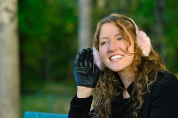 young woman is sitting on the bench in autumn park and listening