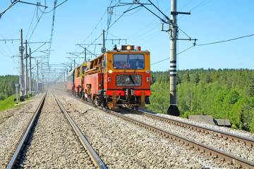 Fototapeta na wymiar Czerwono-pomarańczowy wózek działa przy torach kolejowych w lecie