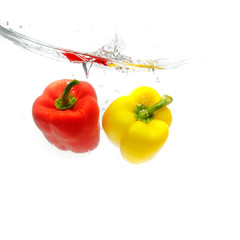 red and yellow peppers splashing into water over white