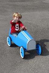 Junge winkend in seinem blauen Tretauto