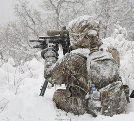 Cold weather hunter covered in snow using a tripod to steady his assault rifle for long shots